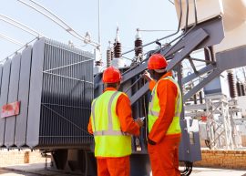 back view of electricians standing next to a transformer in electrical power plant